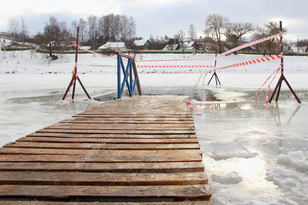 Empty wooden boardwalk planked pathway near empty ice hole on a Sunny frosty winter day, winter ice swimming sport healthy lifestyle