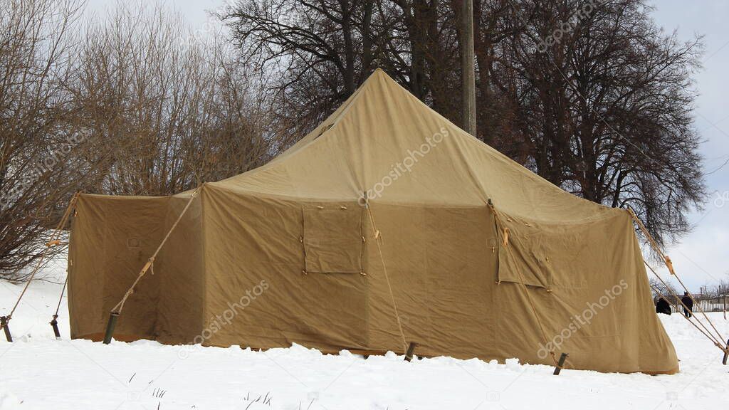 Big khaki military camp tent on white snow on trees background, Russian emergency rescue warming point view at frosty winter day in Park landscape