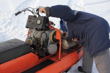 Bir şoför, kış günü beyaz kar üzerinde kapaksız eski Rus servis aracı kar aracını tamir eder.