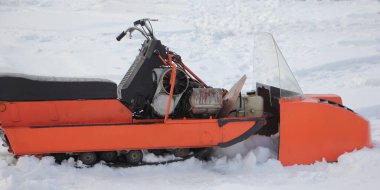 Eski turuncu Rus servis aracı kar motosikleti. Yakın çekim yok. Direksiyon, motor kolu ve yakıt deposu kış günü beyaz kar üzerinde.