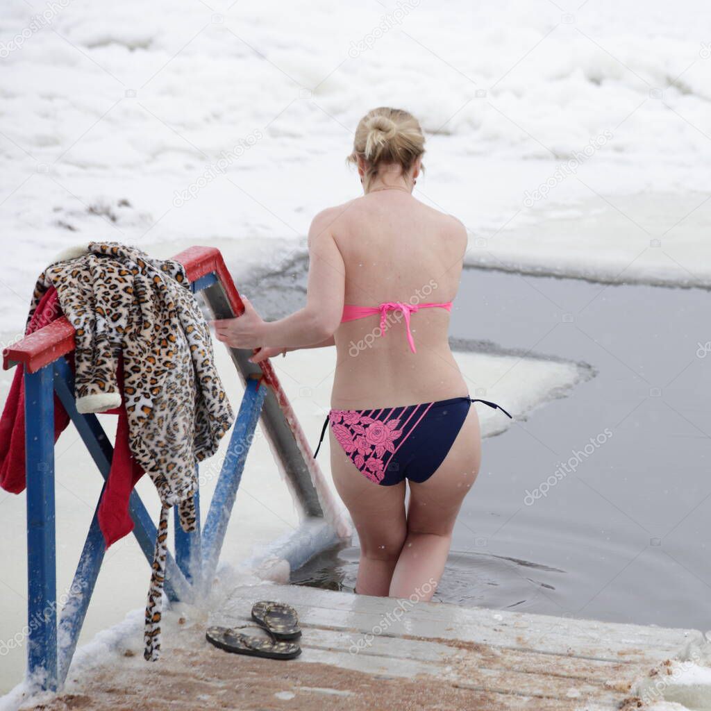 Winter swimming sport, a Russian woman in a swimsuit enters the ice hole water on a Sunny frosty winter day, healthy lifestyle