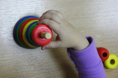 Çocukların renkli ahşap piramit kule mantık oyuncağı. Beyaz çocuğun elinde kırmızı yüzük, çocukların yaratıcılığının erken gelişimi.