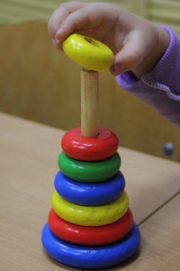 Çocukların renkli ahşap piramit kule mantık oyuncağı. Beyaz bir çocuğun elinde daire şeklinde. Çocukların yaratıcılığının erken gelişimi.