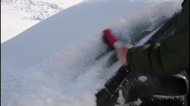 車のフロントガラスから雪を磨く 男の手は雪の後の旅行の準備 晴れた冬の日に車から赤いブラシで雪をきれいにします — ストック動画