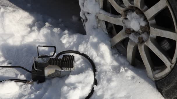 A driver man hand inflates the car wheel with portable electric air tire compressor inflator on white snow background at Sunny winter day, the hose comes off the nipple