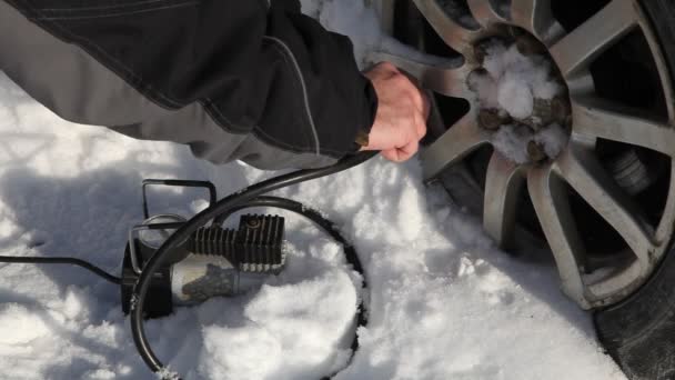 男の手は 晴れた冬の日に白い雪の背景に車のホイールをポータブル電気空気圧縮機タイヤインフレータホースで膨らませ 車両のタイヤの圧力制御 タイヤ自己修復 — ストック動画