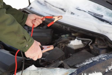 Beyaz eller donmuş araba motorundaki kırmızı ve siyah mineralleri birbirine bağlar. Soğuk kış gününde yedek pil akümülatörü ve kablo ile timsah klipslerini birbirine bağlar.