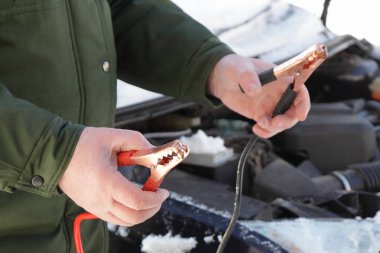 Bir tamircinin elleri, başlangıç kablolarının terminallerini bir araba motorunun arka planına dayandırır soğuk kış gününde ikinci araçtan timsah terminalleri ile hızlı bir şekilde çalıştırır.