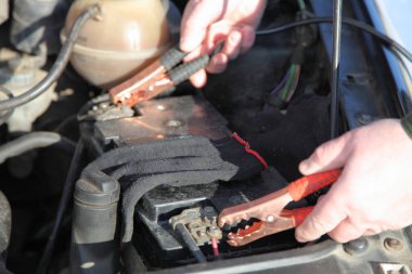 Tamircinin elleri, başlangıç kablolarının uçlarını araba aküsüne bağlar. Donmuş araba motoru düşük sıcaklıkta. Yedek akümülatör ve timsah derisi klipsli kablolarla başlar.