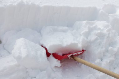 Şiddetli kar yağışı sonrası güneşli bir kış gününde kar altında kırmızı bir kürek. 