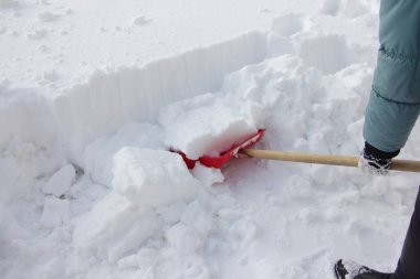Şiddetli kar yağışından sonra, güneşli bir kış gününde kar küreğiyle kar kuyusu kazan bir kadın.