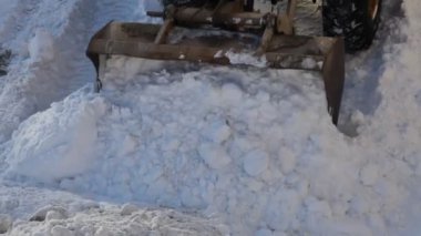 Ağır tekerlekli bir traktor, kış günü yoğun kar yağışı sonrası karayolunda kar küreme kürekli bir karı kaldırır.