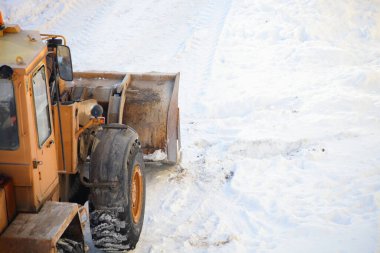 Sarı güçlü tekerlekli bir buldozer traktörü, kar kürekli kar küreme aracıyla kar küreme aracını kış günü yoğun kar yağışı sonrasında kaldırır.