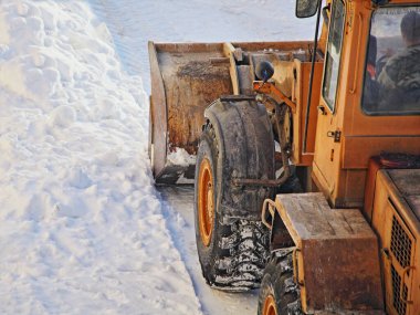 Ağır turuncu tekerlekli bir traktör buldozer, kar kürekli bir karı kaldırır. Karlı bir kış günü, yoğun kar yağışı sonrası, karayolu üzerinde kar küreme küreği kar küreme aracı. Arka taraf yakın plan görüntüsü.