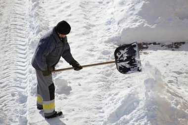 Rus hademe, kış günü yoğun bir kar yağışı sonrasında temizlenmiş bir yolun yanındaki kaldırımdan kürekle kar temizliyor.