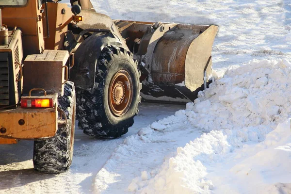 One heavy wheeled tractor removes a snow with scraper shovel blade snowplow on highway road after heavy snowfall at Sunny winter day, top front view close-up