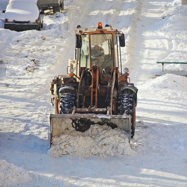 One powerful wheeled bulldozer tractor removes a snow with scraper shovel blade snowplow on road with cars on roadside after heavy snowfall at winter day, top front view