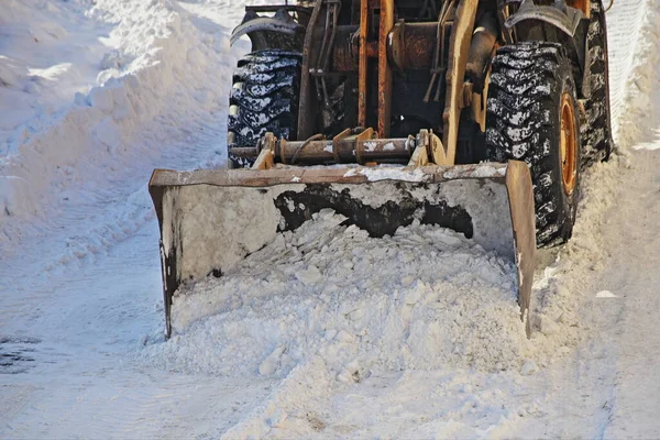 One powerful wheeled bulldozer tractor removes a snow with scraper shovel blade snowplow on road after heavy snowfall at winter day, top front view closeup