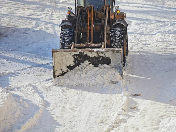 One heavy wheeled tractor removes a snow with scraper shovel blade snowplow on highway road after heavy snowfall at Sunny winter day, top front view close-up