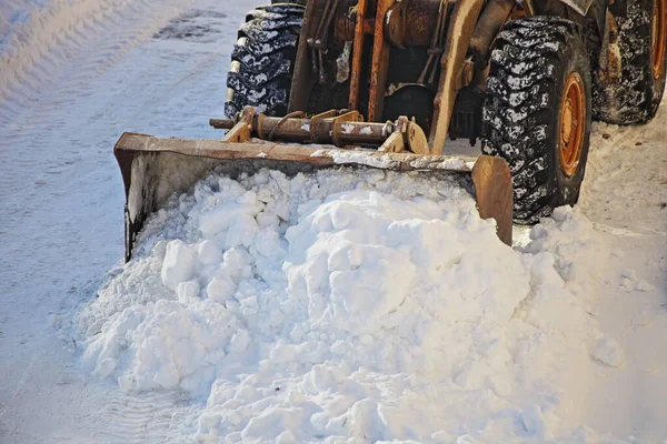One powerful wheeled tractor removes a snow with scraper shovel blade snowplow on road after heavy snowfall at winter day, top front view closeup