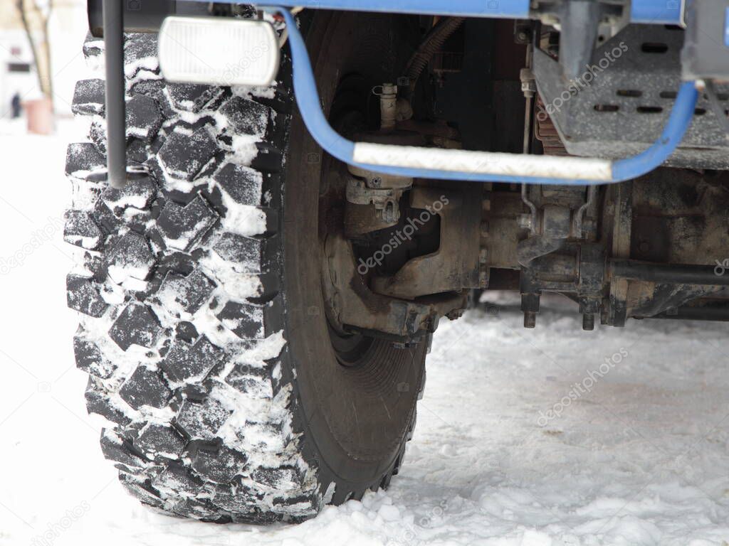 Off-road truck big wheel, anti fog lamp, front axle, steering knuckle, brake mechanism, anti-roll bar, front suspension elements and right tire on snow road, 4x4 vehicle construction close up