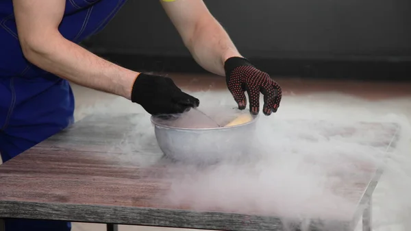 Male magician\'s hands in black gloves place a banana in a bowl of liquid nitrogen on the table close up, fast cooling of the food