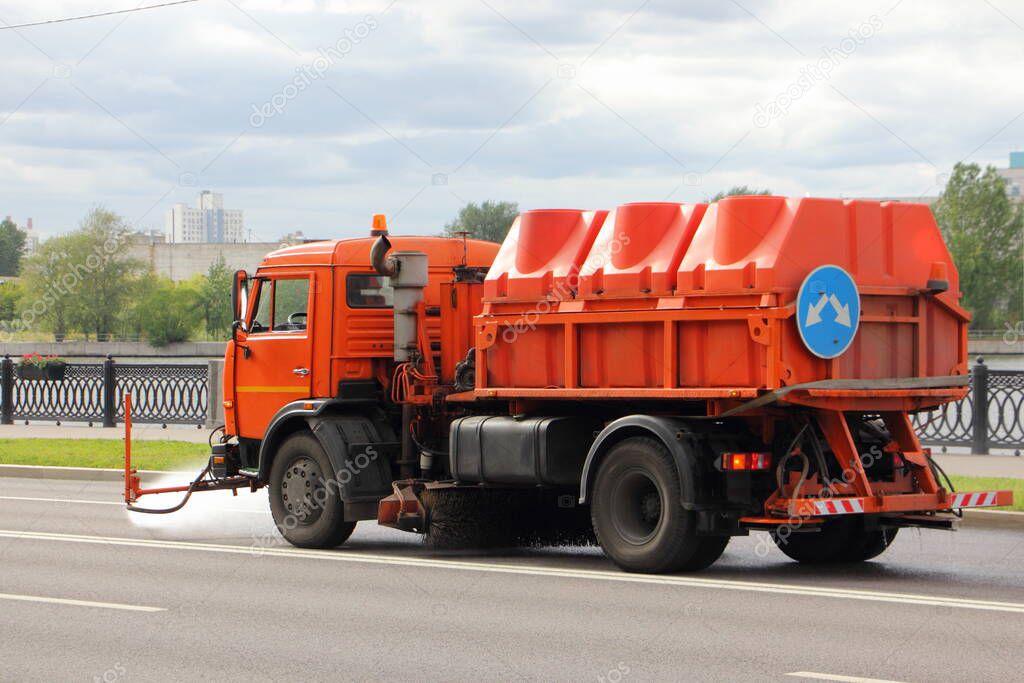 New Russian orange watering machine truck pours asphalt road, street washing in Moscow, city improvement by municipal services on a sunny summer day