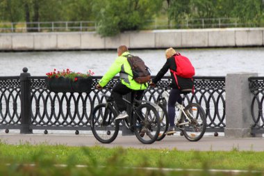 Bir yaz günü Moskova Nehri 'nin arka tarafında asfaltlanmış Nagatinskaya seti üzerinde kasksız bisiklet süren iki bisikletçi. Moskovalıların kentsel aktif yeniden yaratımı