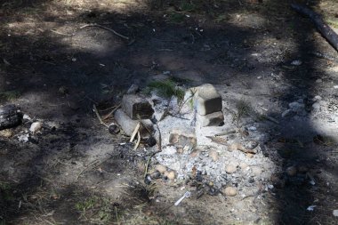 Terk edilmiş şöminenin gri külleri. Yerde beyaz tuğlalar. Güneş gölgeleri, açık hava piknik eğlencesi, boş bir kamp yeri şöminesi güvenliği.