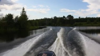 Sürat teknesi nehir suyunda döner. Yaz mevsiminde arka planda yuvarlak keelwater izleri olur. Köpüklü trenin POV arkası görünür.