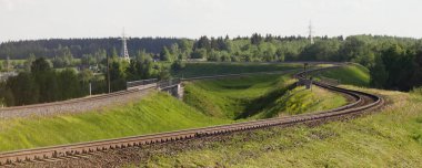 Beautiful empty windy railroad track turn on green grass hills at Sunny summer day on forest on horison, European countryside landscape