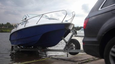 4x4 siyah bir araba mavi-beyaz trimaran motorlu teknesini nehir suyuna doğru beton kaydırak üzerinde çekiyor. Nehirde aktif eğlence başlamadan önce tekne kalkıyor.