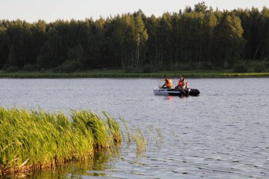 Turuncu can yelekli iki balıkçı şişirilebilir motorlu ve 9.9 beygir gücünde bir motorda yüzüyorlar. Bu da yaz günü çimenli sahil arka planında nehri yeniden canlandırmak ve kayıt gerektirmiyor.