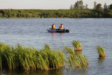 Turuncu can yelekli iki balıkçı şişme motorlu 9.9 beygir gücünde yüzüyorlar. Bu da yaz günü otlak arka planda Rus nehrinde kayıt ve dinlenme gerektirmiyor.
