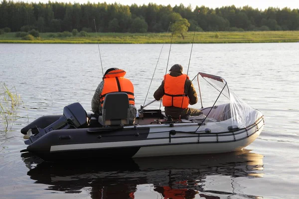 オレンジライフジャケットの2人の漁師は 夏の日にロシアの川で釣竿で登録 レクリエーションを必要としない9 9馬力の船外機と現代のインフレータブルモータボートに浮かびます — ストック写真