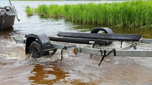 Empty boat trailer leaving the water after launching a motor boat into the water at summer day on river green grass background