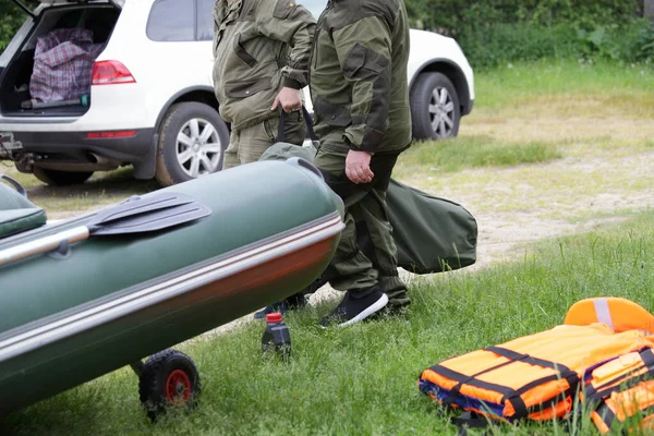 二人の男は 夏の日にインフレータブルボートと車の背景に袋に船外機のモーターを運びます 水の上の旅行の準備 — ストック写真