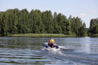 Turuncu can yelekli bir adam şişirilebilir motorlu dış motorlu yeşil ağaçların üzerinde yüzen bir adam Sunnny yaz gününde suda aktif bir eğlence.