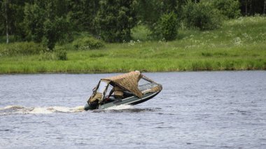 Tenteli ve motorlu şişirilebilir motorlu tekne hareket ediyor. Çimenli, uzak kıyılarda ve yeşil ağaçlarda süzülüyor. Yazın arka planda, su araçları açık havada seyahat ediyor.