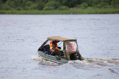 Yaz günü, tenteli ve dış motorlu şişirilebilir motorlu tekne çimenli, uzak sahil arka planında yüzüyor. Su teknesi balıkçılığı turizmi.