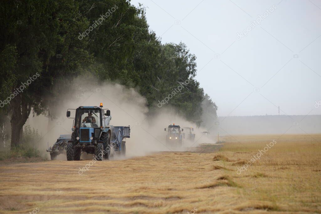 A many wheeled tractors with harvester trailers fast drive on dusty road on harvested linen field edge, linum harvesting in Europe at summer day