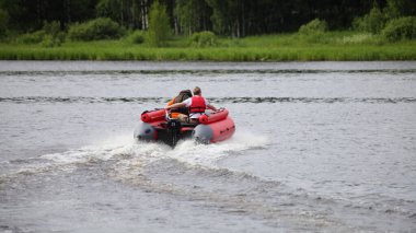 Şişme motorlu ve kırmızı ceketli bir adam hızla yeşil orman arka planında suda yüzüyor. Rusya 'nın güzel nehir manzarası.