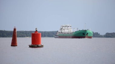 Rus yeşil kargo gemisi suda yüzüyor, kırmızı şamandıra ve orman bankasının arka planında yaz günü, Volga nehrinde navigasyon, nakliye lojistiği