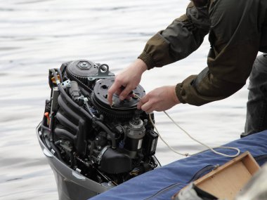 Tekne çalışanı, teknenin kaputu olmadan teknenin dış motorunu çalıştırıyor. Acil durum motoru halatla çalışıyor.