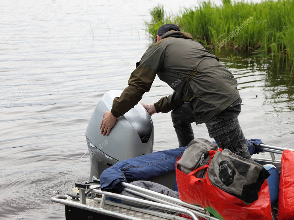 Boater man hands removes the hood of a 50 hp four stroke outboard motor on transom of boat, repair and maintenance boat engine