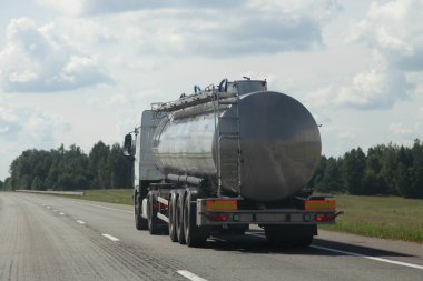3 eksenli gri varilli kamyonet sağ şeritte boş banliyö yolunda Sunny yaz gününde mavi bulutlu gökyüzü arka planında, Avrupa 'daki tüm kullanışlı sıvı ulaşım lojistiği