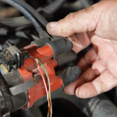 Araba motoru ateşleme sistemi teşhisi, tamircinin elinde tutuş kontağı ve eski araba motoru kabloları.