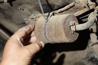 Eski arabanın yakıt sistemini kontrol ediyorum. Bir adamın eli kullanılmış arabanın altındaki değiştirilebilir paslı yakıt filtresini kontrol ediyor.