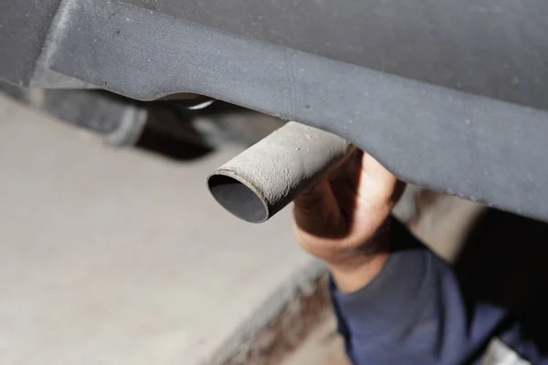 Test the exhaust system of the used car - a man\'s hand checks the exhaust silencer pipe clamp fastening under the bottom of the vehicle