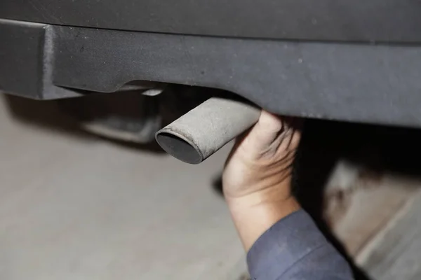 Checking the exhaust system of the old car - a man\'s hand checks the exhaust silencer pipe under the rear bumper of the used car